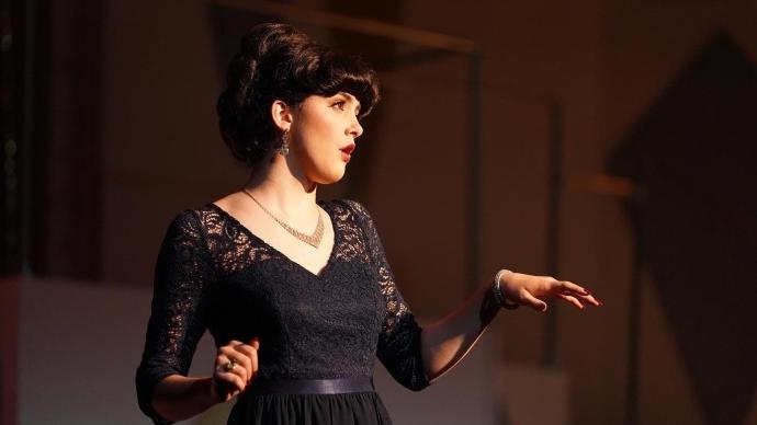 Eva Tatum sings a in a musical, wearing a black dress